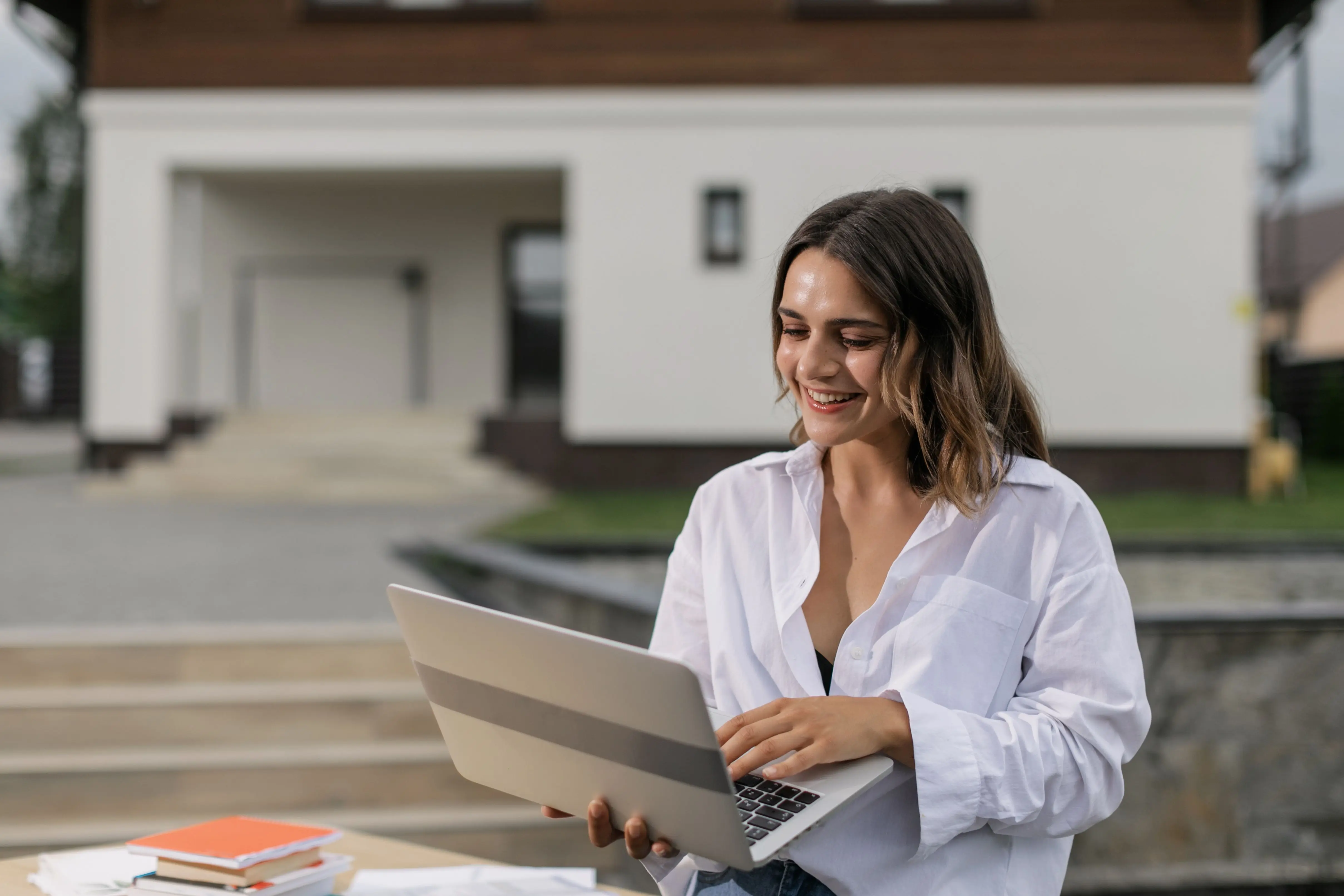 Courtière immobilière souriante travaillant sur un portable devant une maison